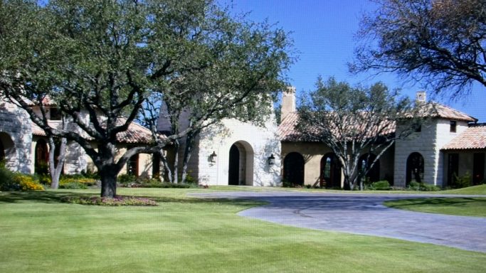Spacious estate with stone architecture, green lawn, and trees under blue sky.