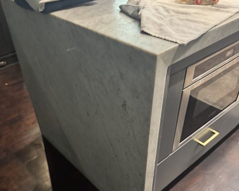 A modern kitchen countertop with a marbled surface and a microwave below.