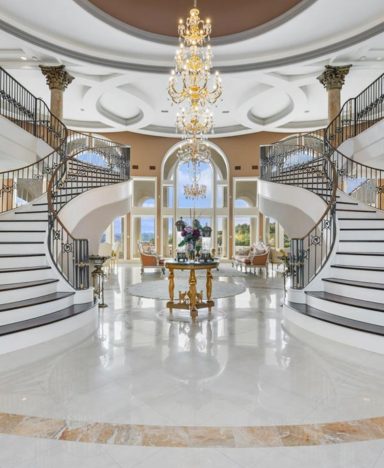 Luxurious foyer with grand staircase, elegant chandelier, and large windows.
