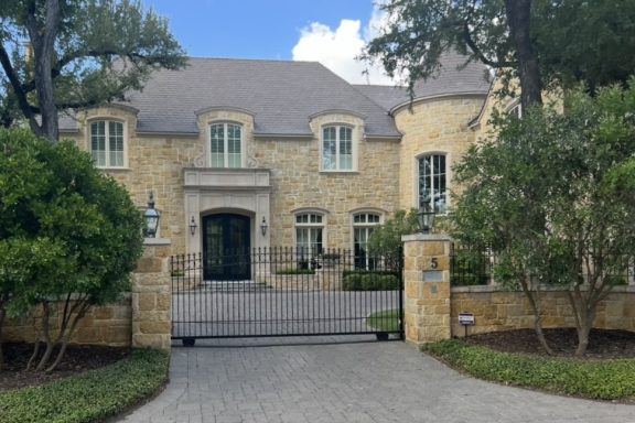 Elegant stone mansion with large windows, manicured landscaping, and a driveway.